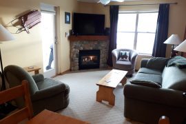 Living room of condo with gas fireplace, TV and bright windows. Top floor for ultimate quiet and a corner unit with large balcony and BBQ. Pet-friendly, free parking and great views of the Adventure Park.
