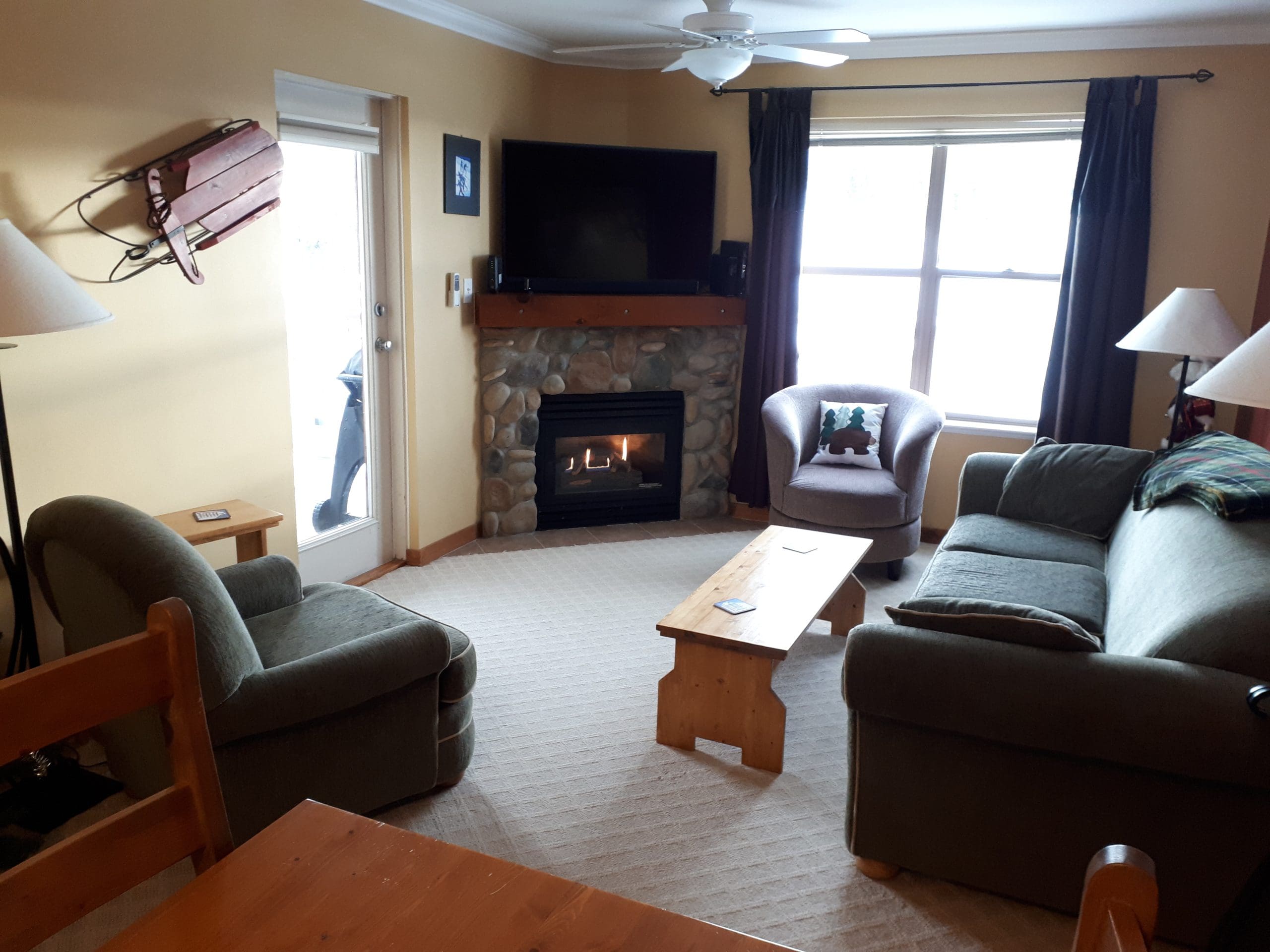 Living room of condo with gas fireplace, TV and bright windows. Top floor for ultimate quiet and a corner unit with large balcony and BBQ. Pet-friendly, free parking and great views of the Adventure Park.