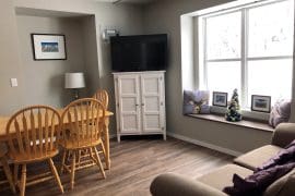 Living room with dining table, fireplace and TV. Cozy one bedroom ground floor suite with great access to the skiway and trails to start your day. Pet-friendly, brand new BBQ and semi-private hot tub.