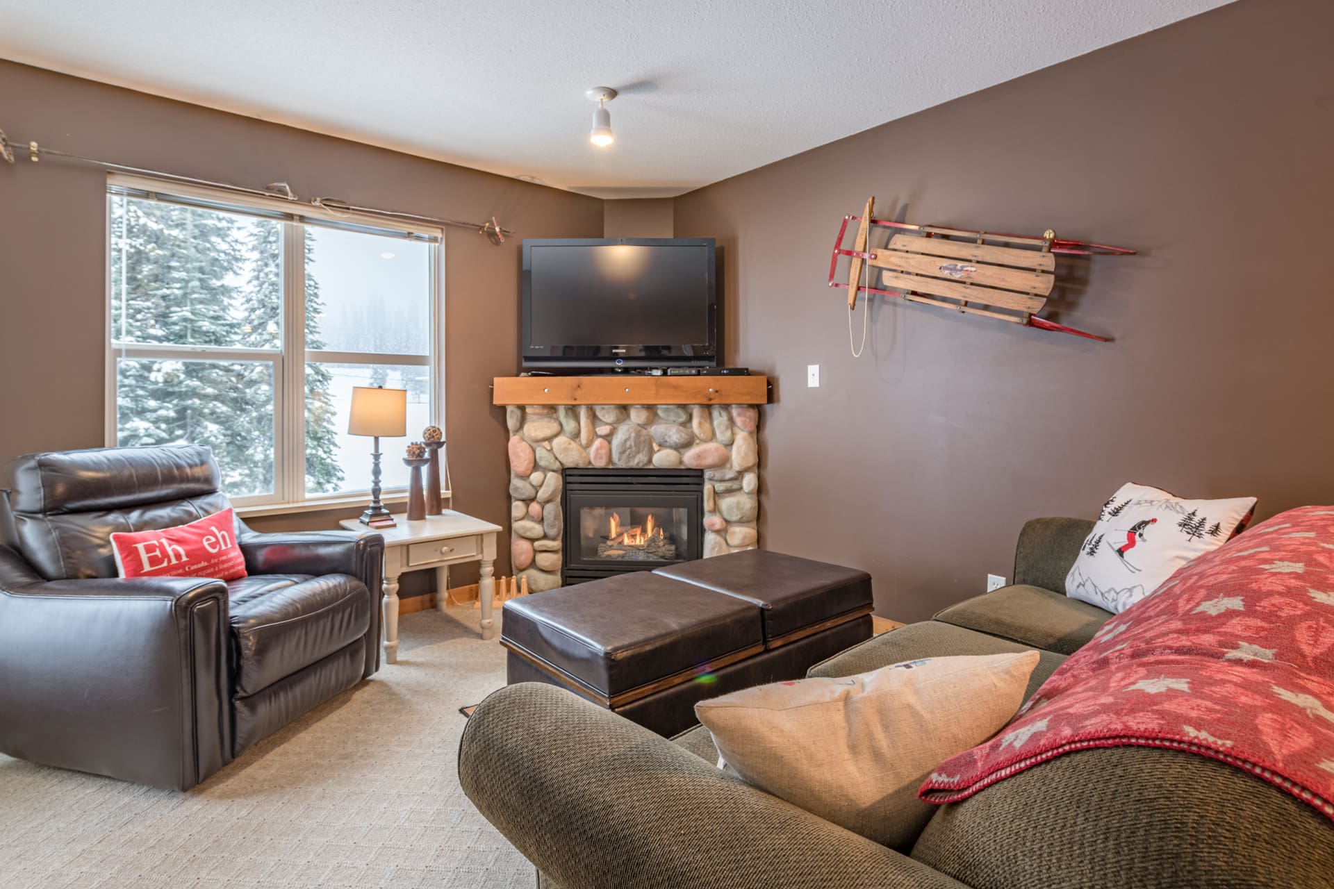 Living room of top floor condo with bright open windows, updated furniture, gas fireplace, TV, large balcony with BBQ, and amazing ski access directly slopeside.